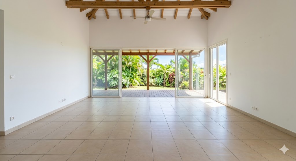 Salle vide avec carrelage, poutres apparentes et grandes baies vitrées donnant sur jardin.