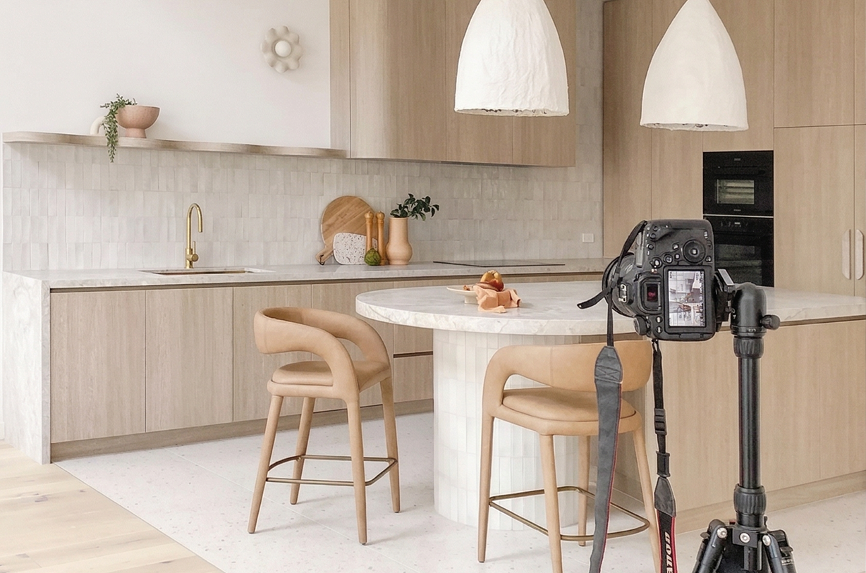 Cuisine moderne avec îlot central, tabourets en cuir et appareil photo sur trépied.